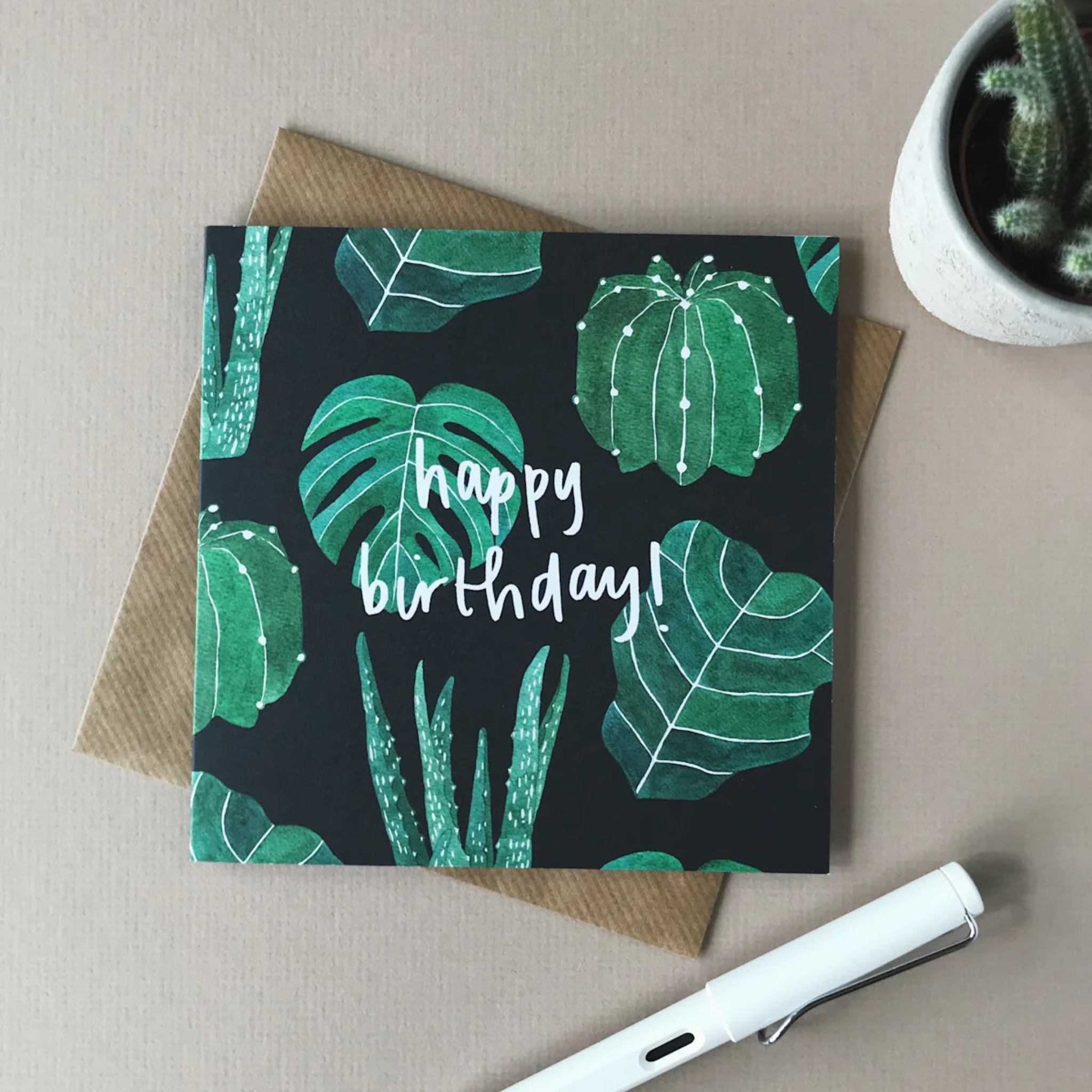 Dark green card with green watercolour plants and leaves with the words &quot;Happy Birthday!&quot; in a white script font.