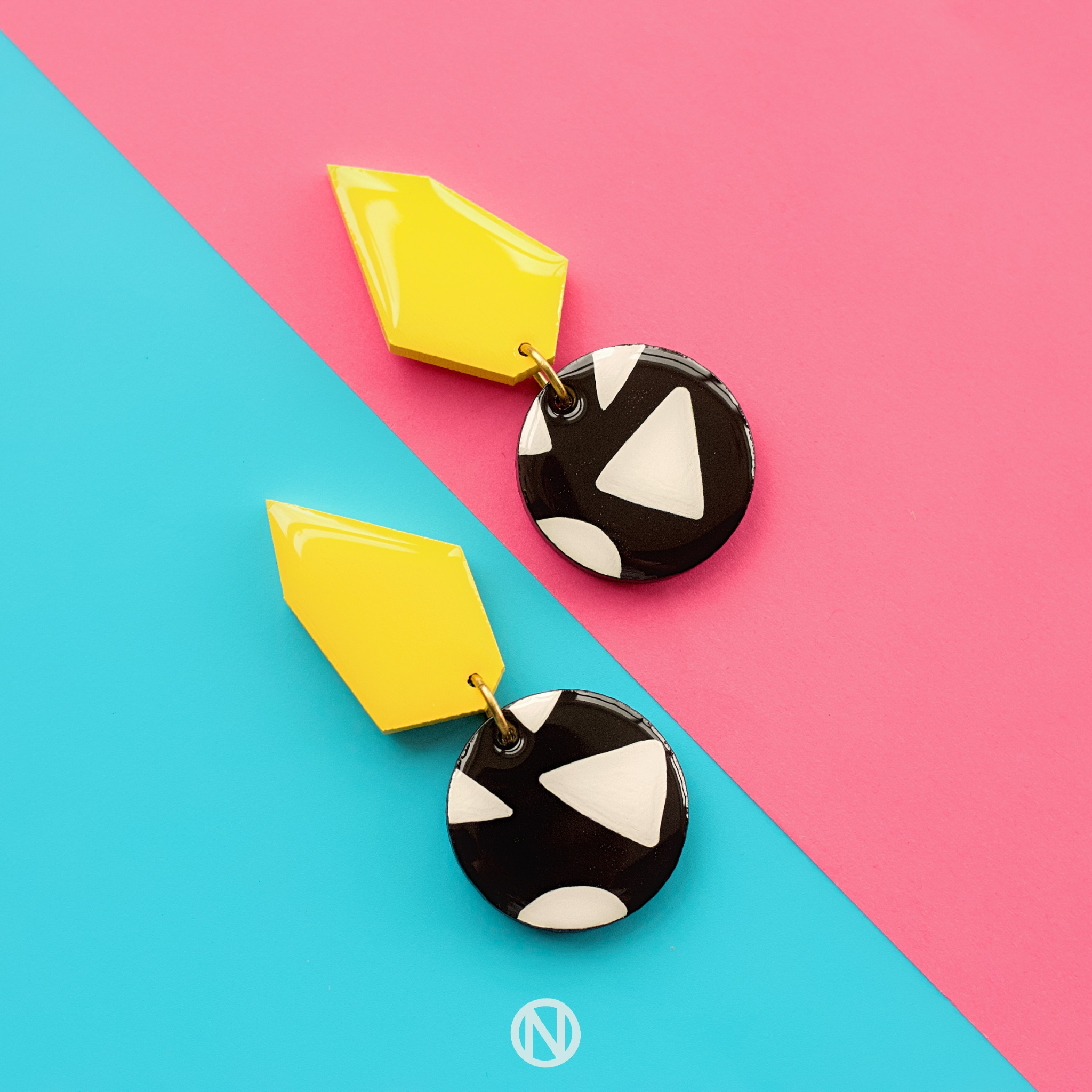 Earrings with a yellow geometric shape on top, and a black and white circle section at the bottom with a triangle pattern.