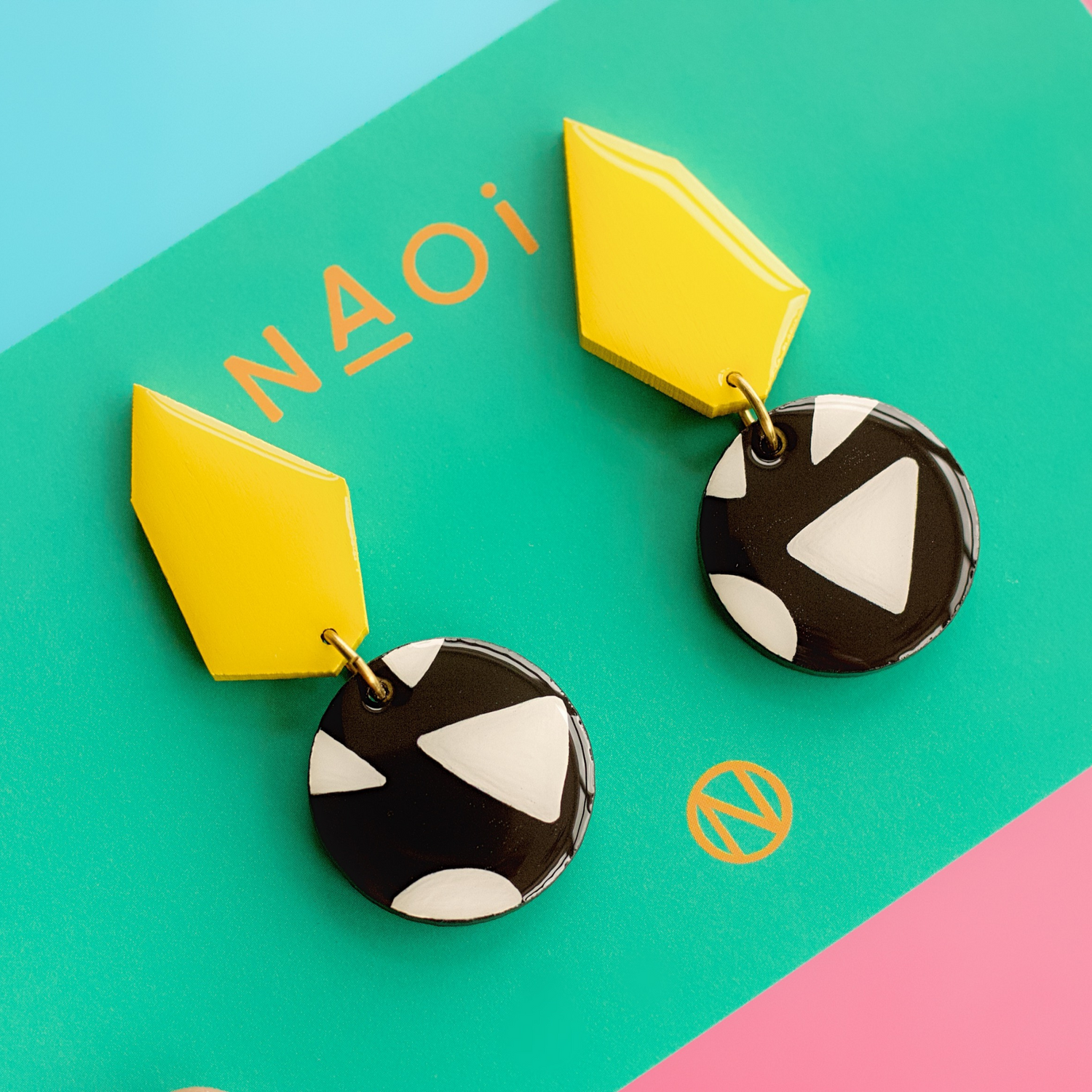 Earrings with a yellow geometric shape on top, and a black and white circle section at the bottom with a triangle pattern.