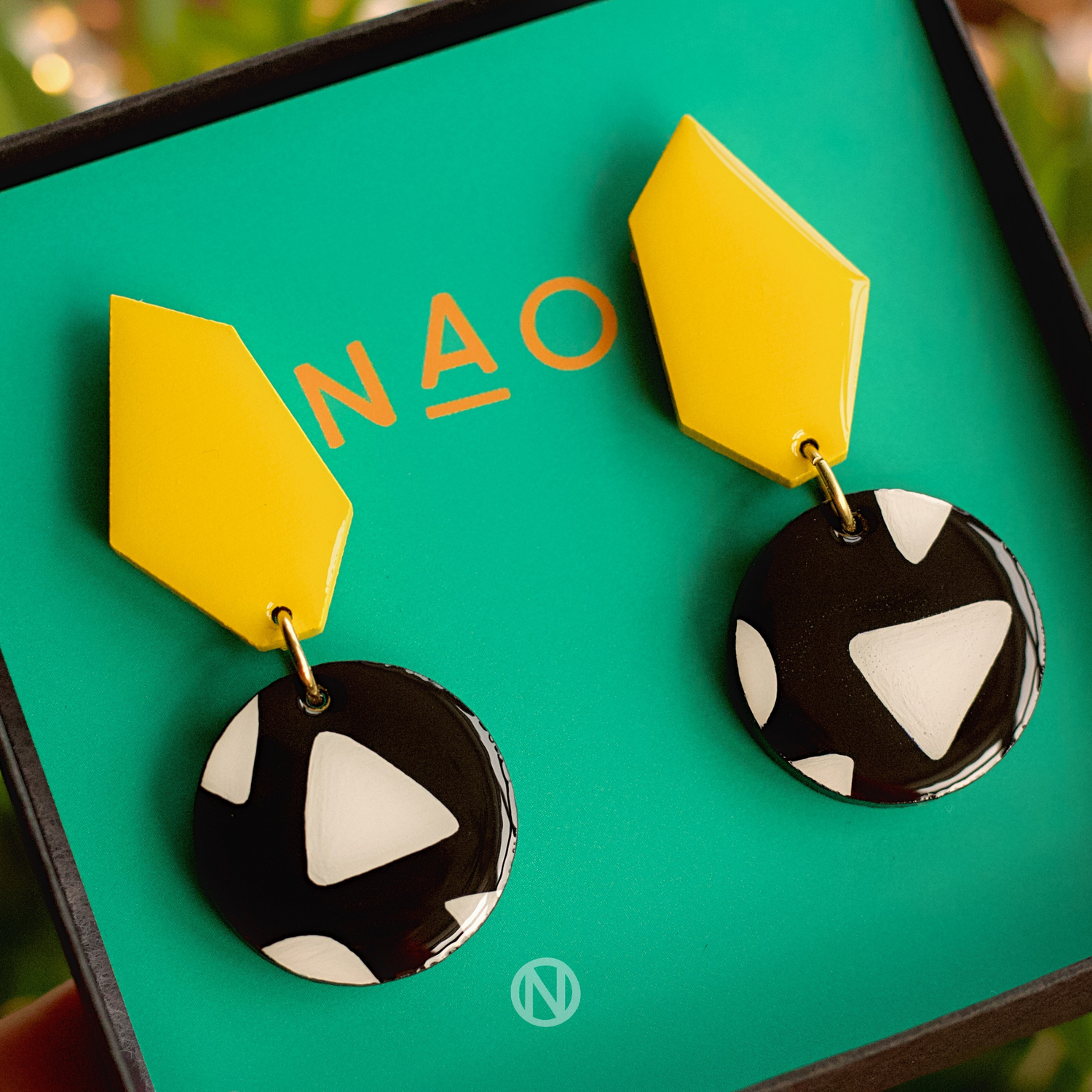 Earrings with a yellow geometric shape on top, and a black and white circle section at the bottom with a triangle pattern.