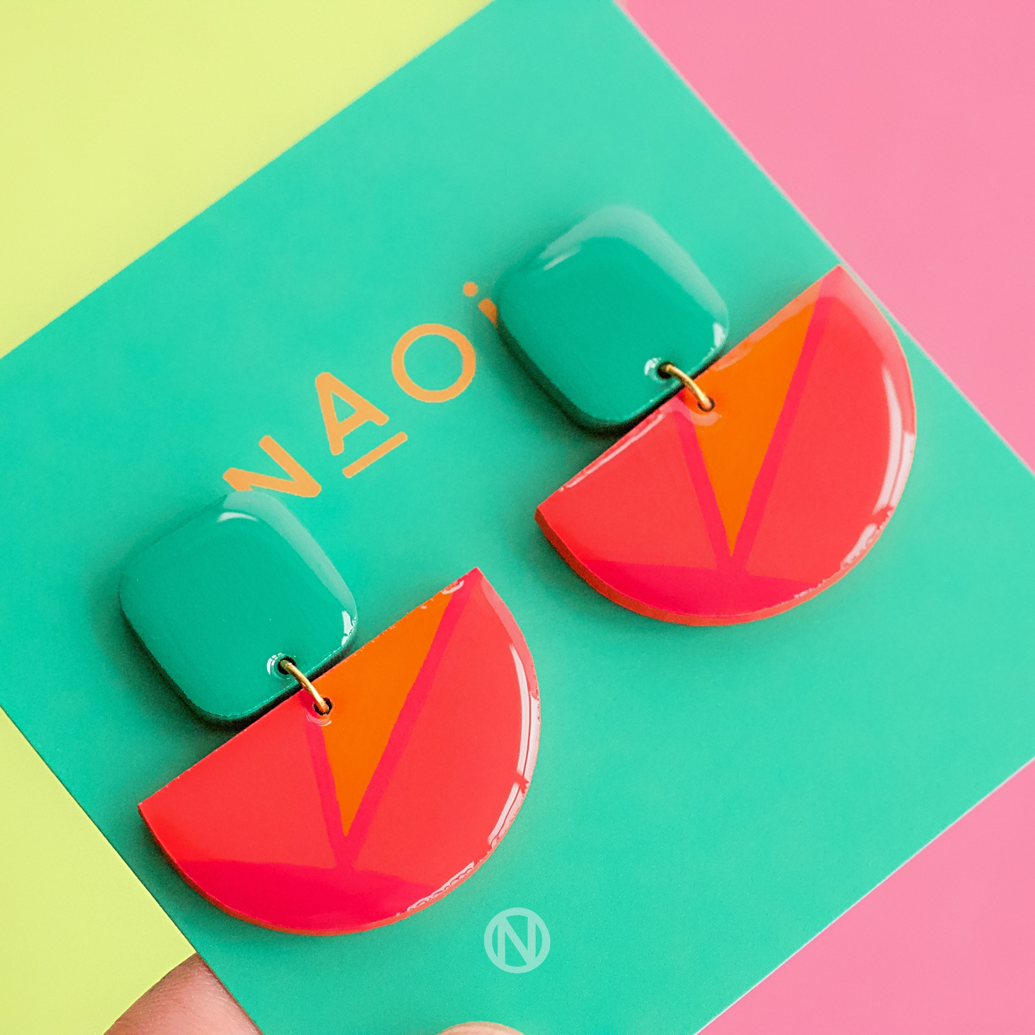 Earrings with a turquoise rounded rectangle shape on top, and a pink and orange semi circle section on the bottom.